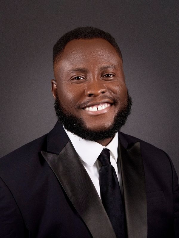 Professional headshot of Benjamin Fakunle wearing a black suit and smiling at the camera.