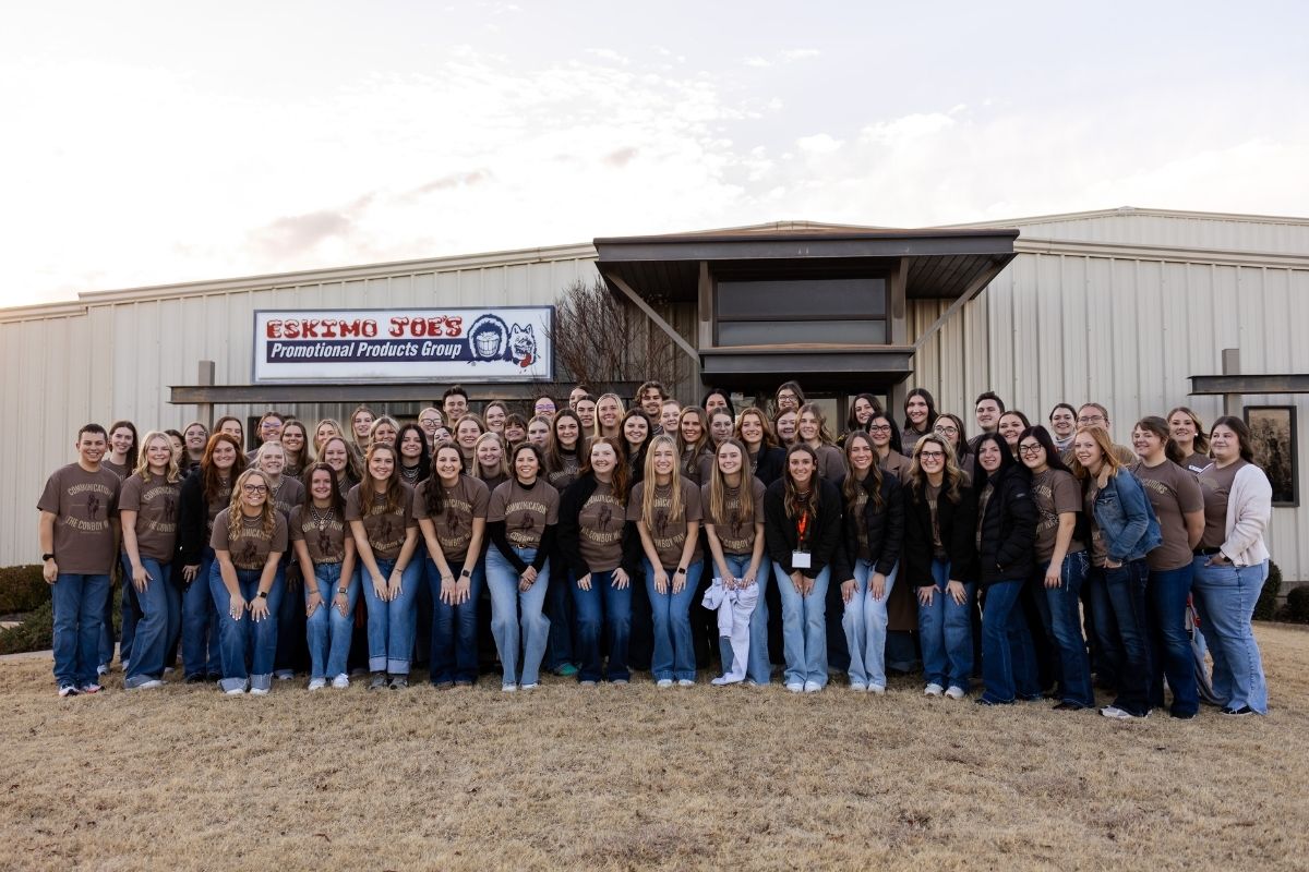 pdc_1200x800px.jpg Group photo of PDC attendees posed in front of a tan metal building. All attendees are wearing the tan PDC group shirt, and jeans, many of them are also wearing jackets.