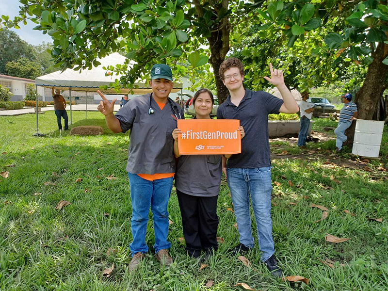 Three students display a #FirstGenProud sign.