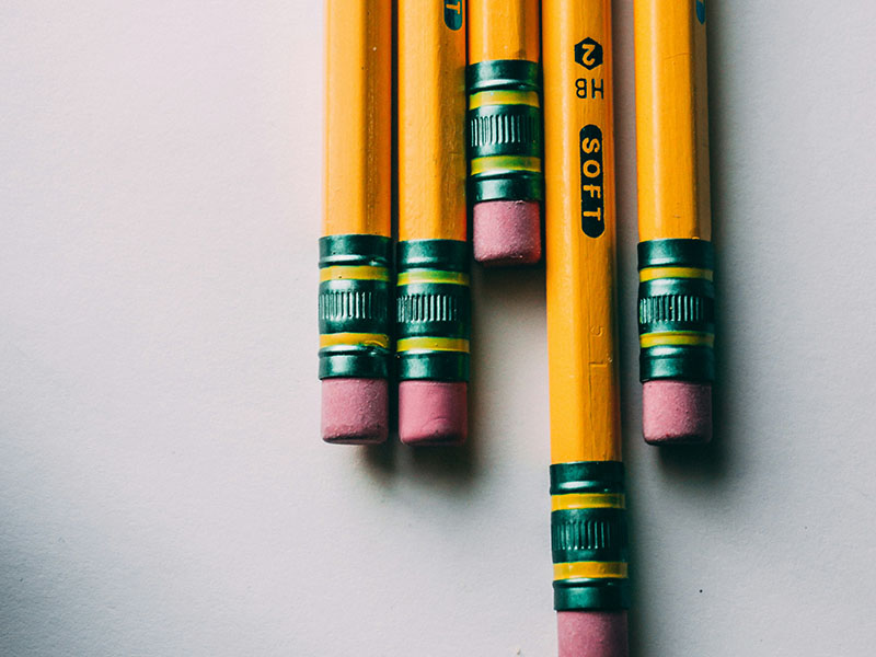 Six yellow pencil next to each other with a red eraser.