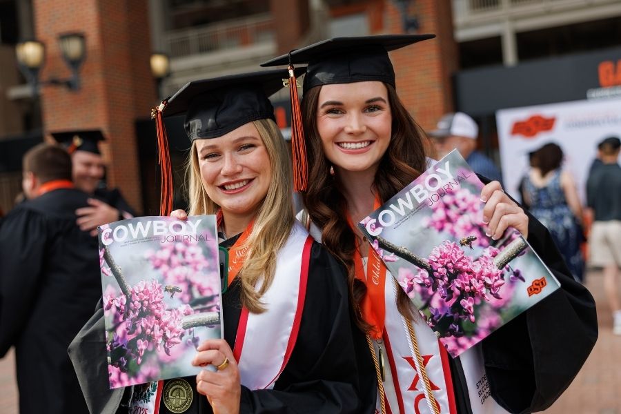 Two students at graduation holding the new Cowboy Journal, showing off the cover