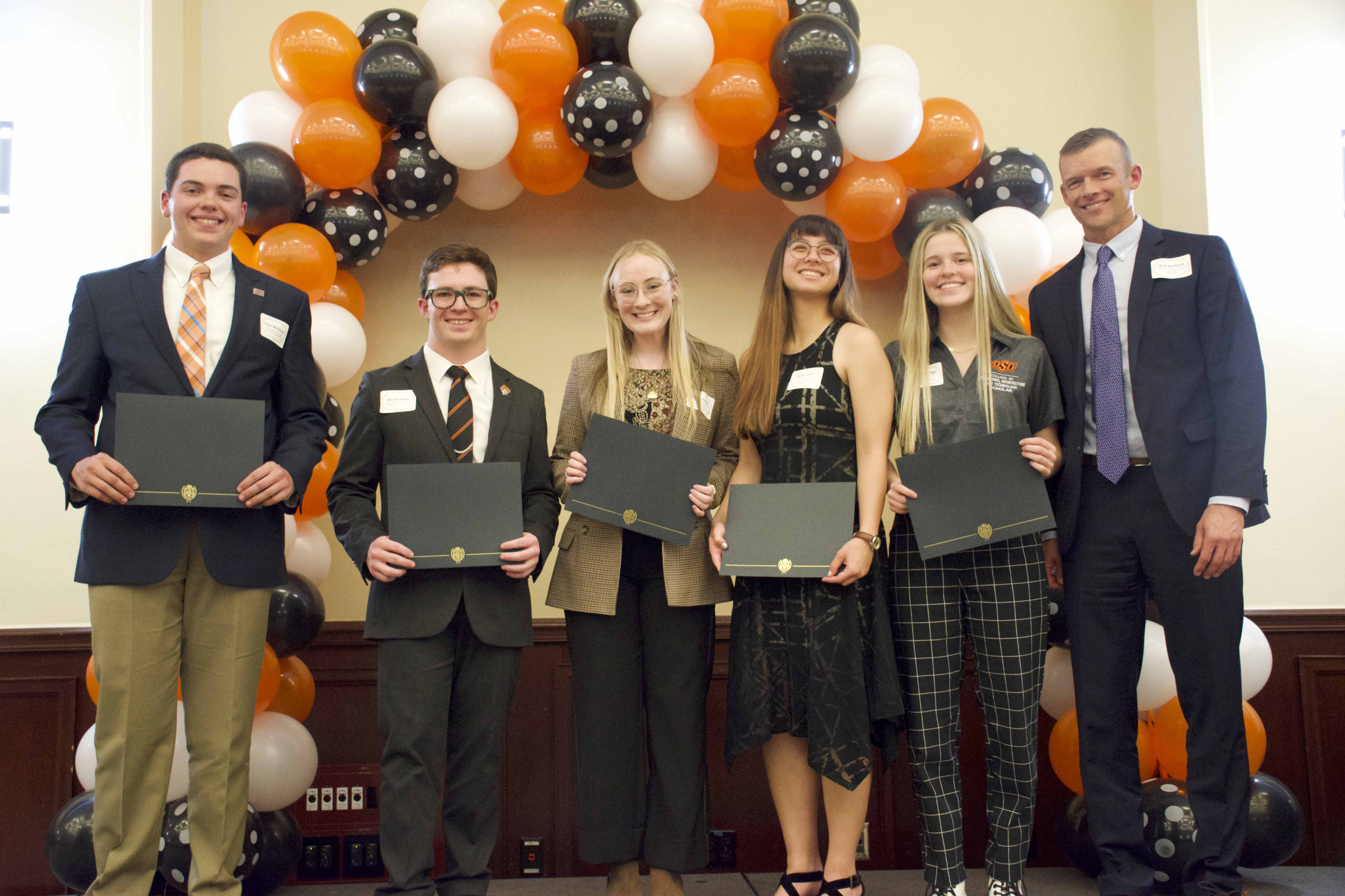 A group of students holding certificates in front of a balloon arch. A group of students holding certificates in front of a balloon arch.