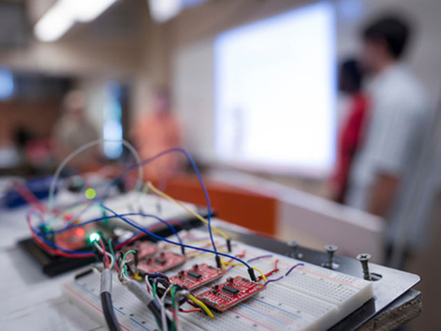 A circuit board with wires coming off it in the foreground.