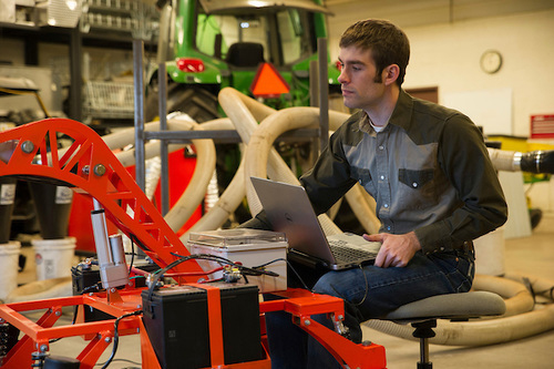 student is sitting on machinery while analyzing data on a laptop. student is sitting on machinery while analyzing data on a laptop.