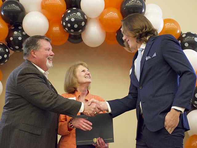 A man and woman shaking hands with a boy receiving a scholarship. A man and woman shaking hands with a boy receiving a scholarship.