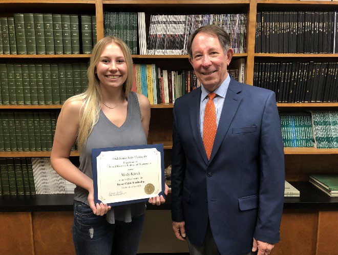 Molly Koeck is accepting her award from Jim Ansley in front of a book shelf.
