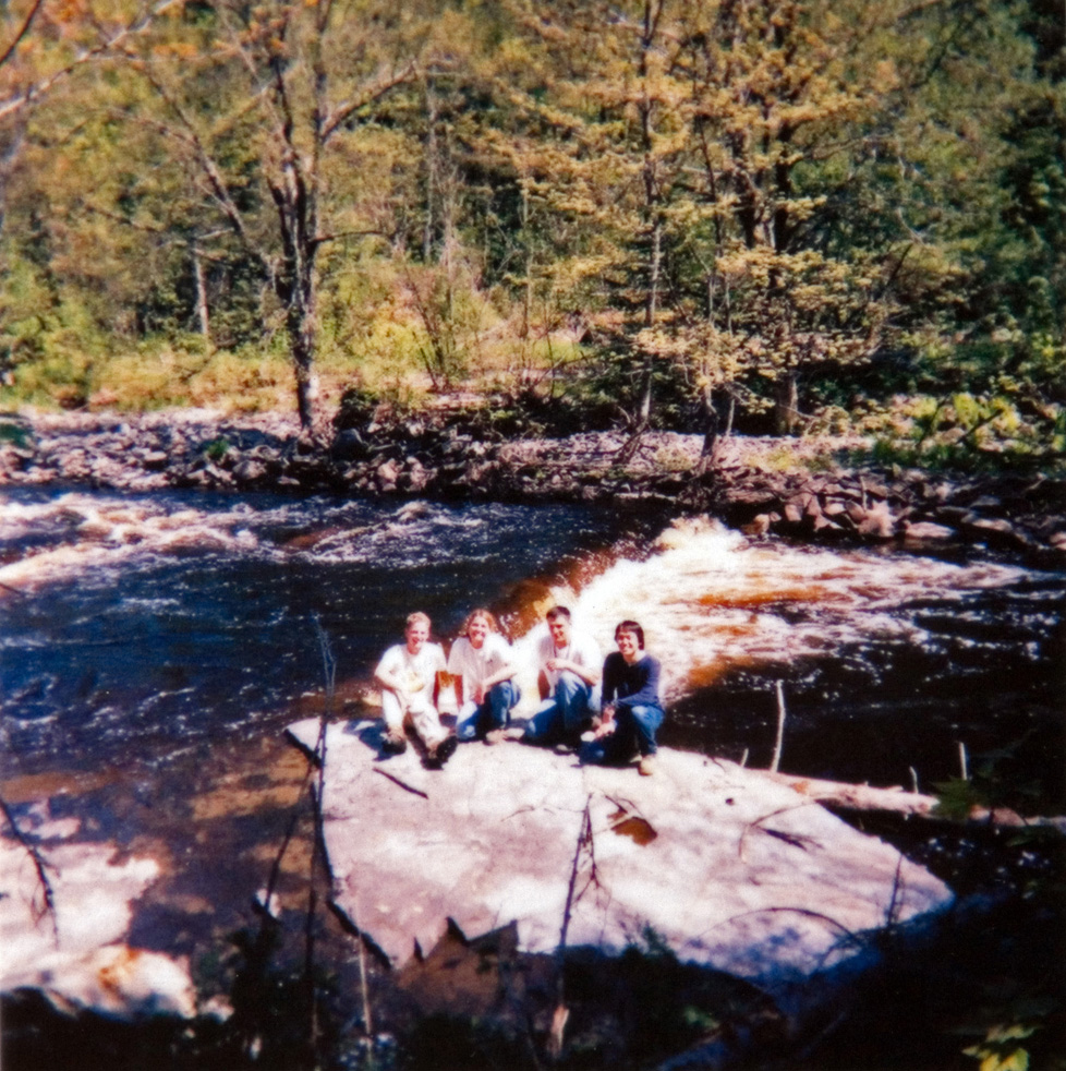A group of individuals sitting on a rock in amidst a stream of water.
