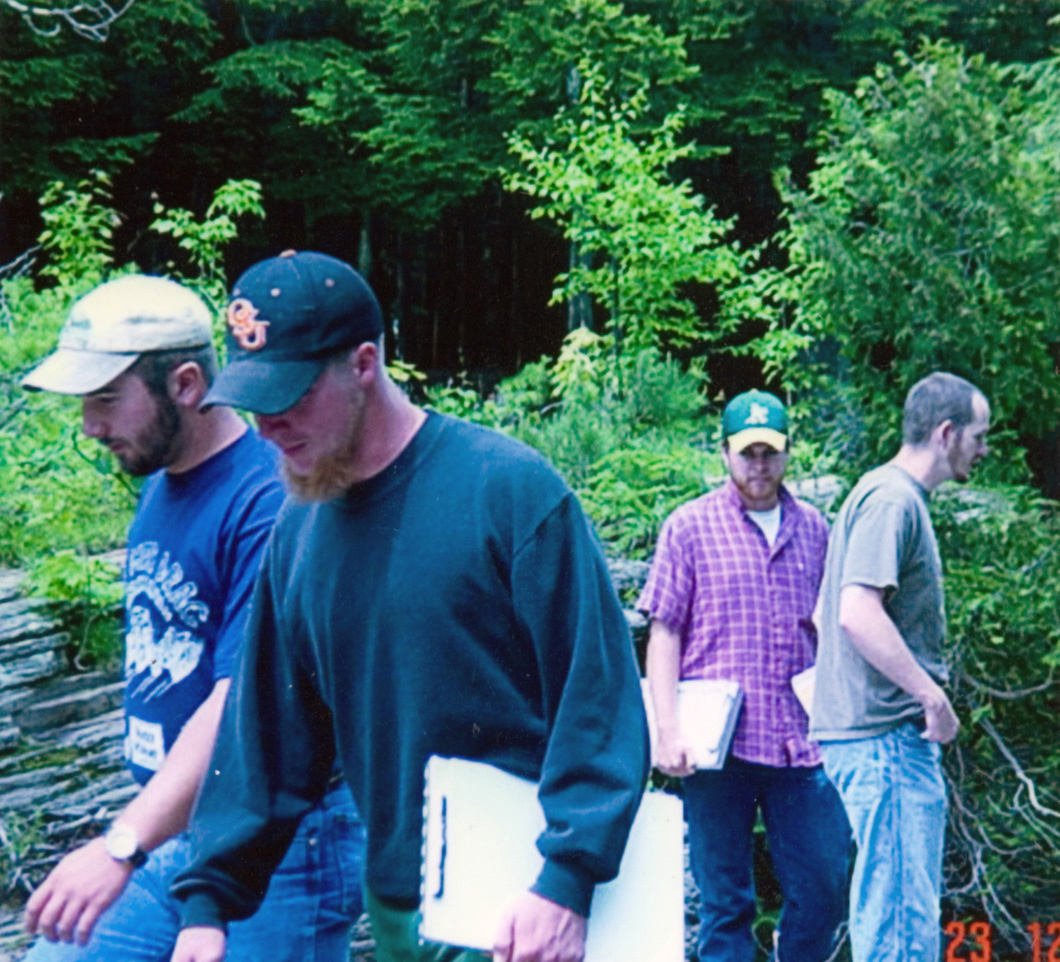 A group of four individuals out on a search in a green forest with clipboards in hand.