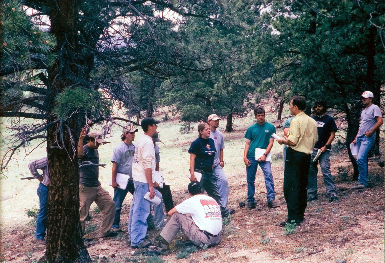 A group of students all holding binders as they gather together to listen to an instructor.