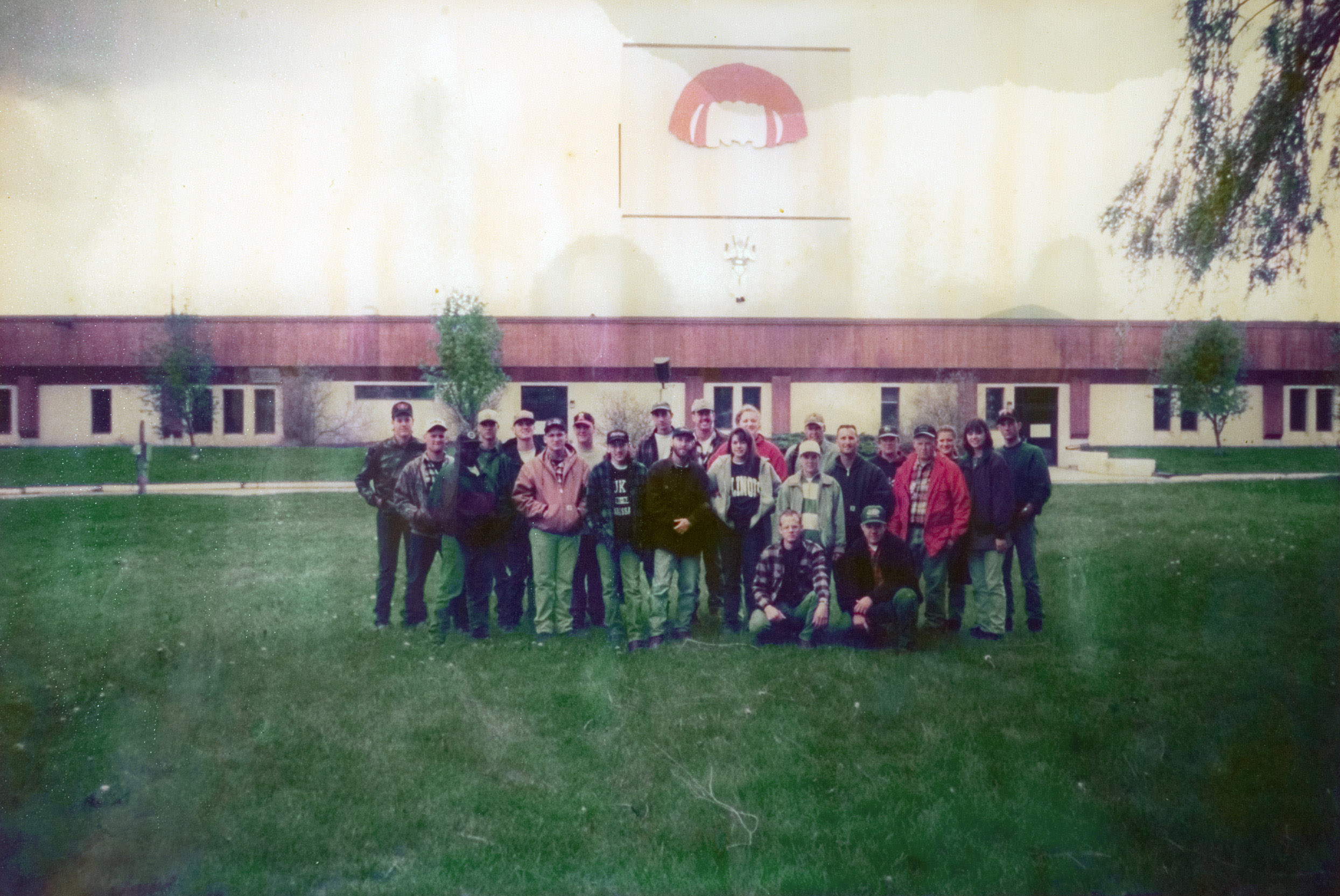 A group of 23 students from the Forestry Camp standing outdoors on a field of green grass as they pose for thier photo to be taken.