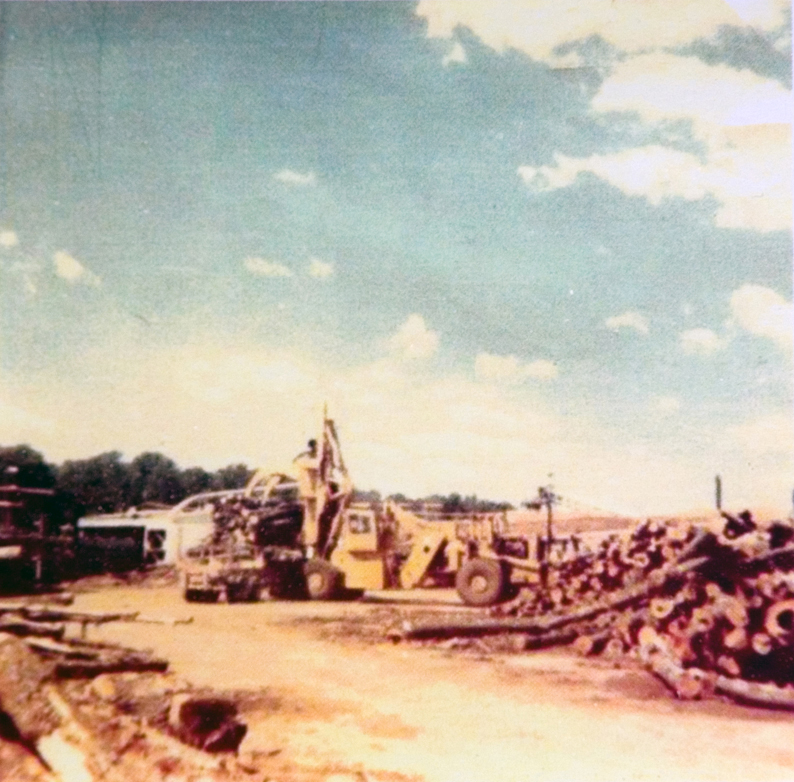 A tractor ouside next to cut down tree trunks.