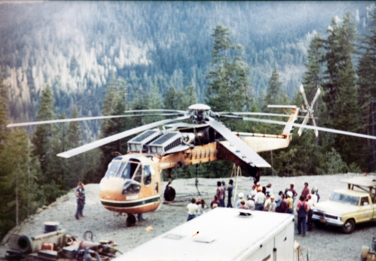 The camp group gathers near a helicopter.