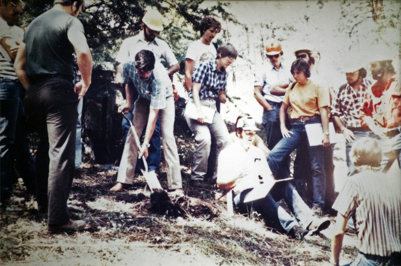 The camp group listens to instruction while one student begins digging.