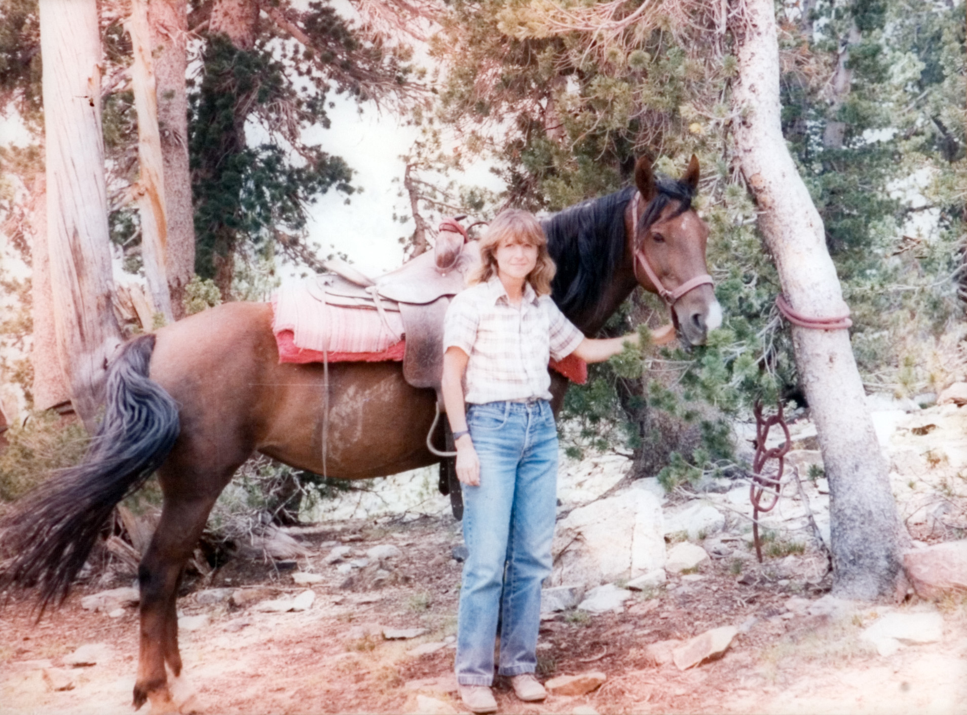 Student smiles for the camera next to her horse in the woods. 