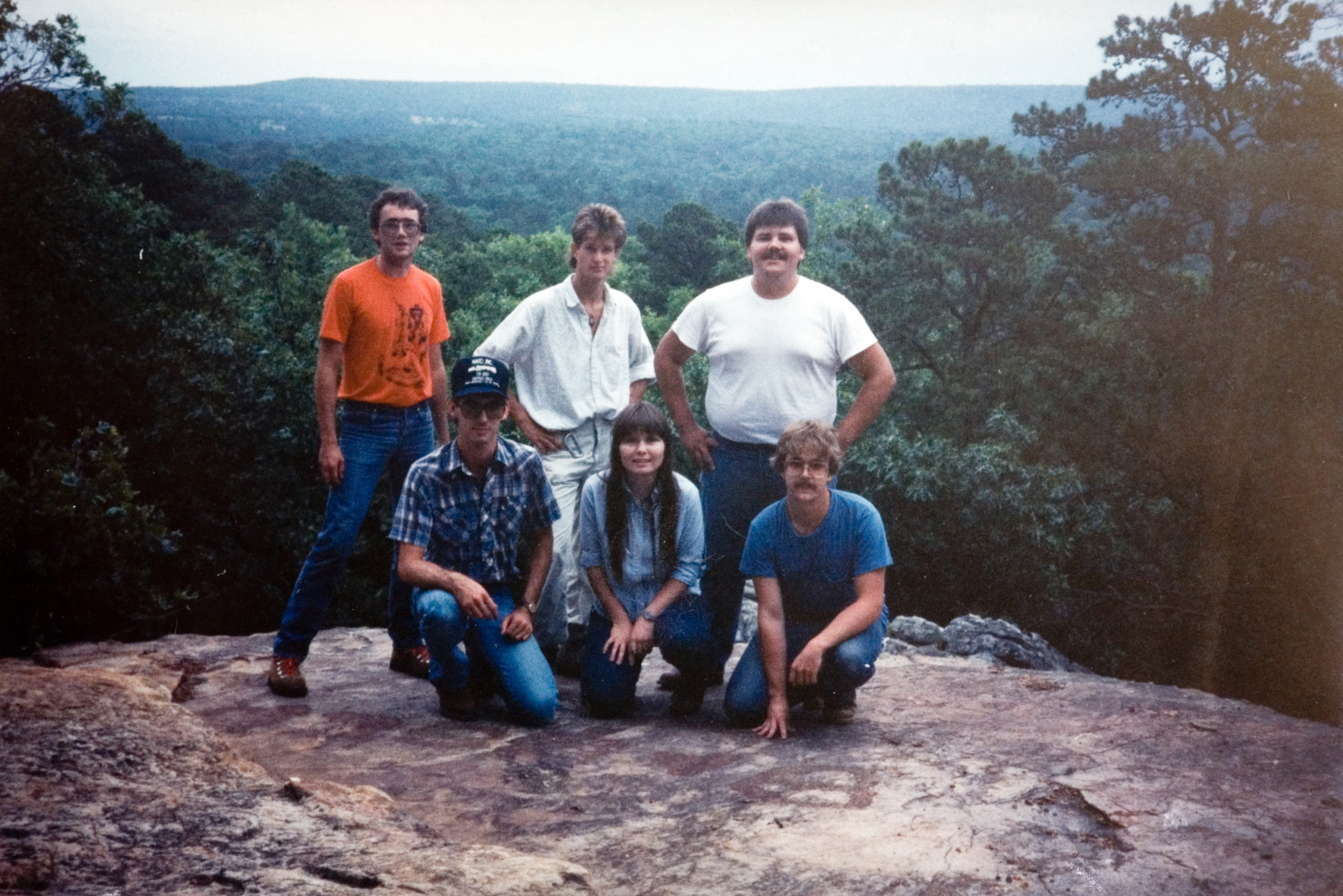 Six students pose for a photo on the top of a cliff in the forest.