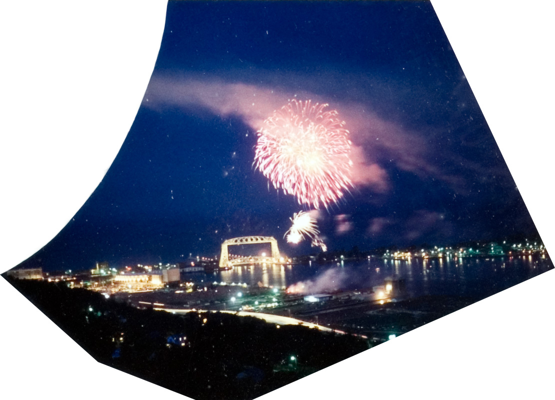 A top view a city next to a lake during a firework show at night.