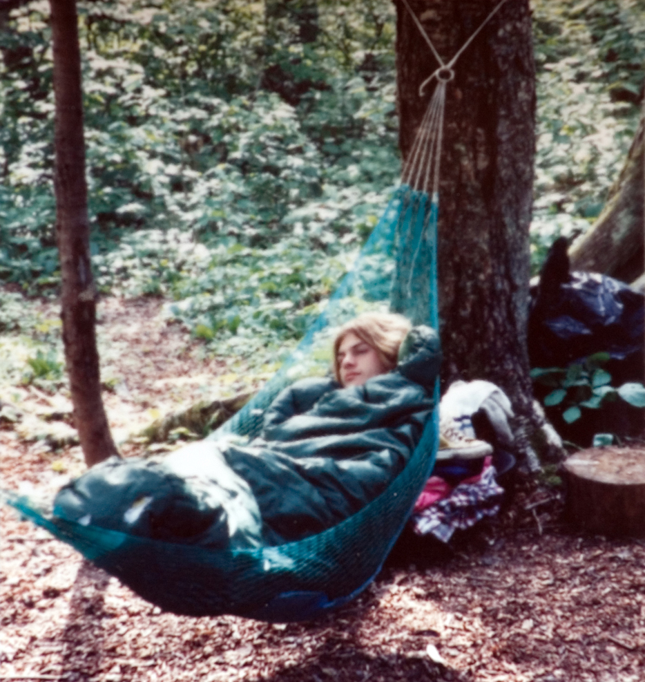 A student snuggles up in a hammock for a nap in the woods. 