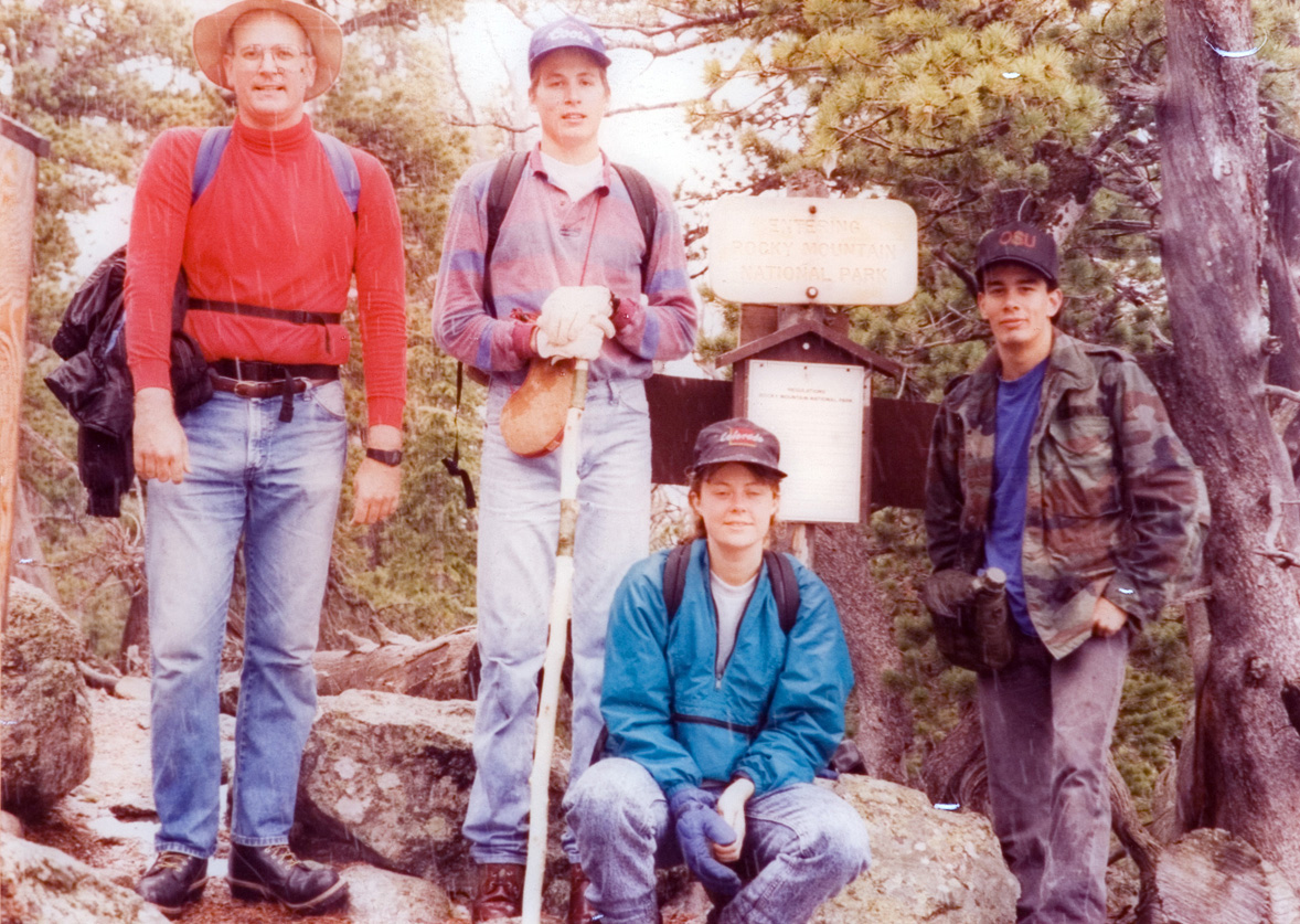 Three students and an instructor pose for a photo at a trail marker.