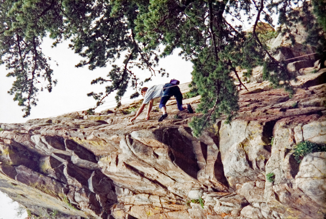 A student climbing on top of a cliff to reach the edge.