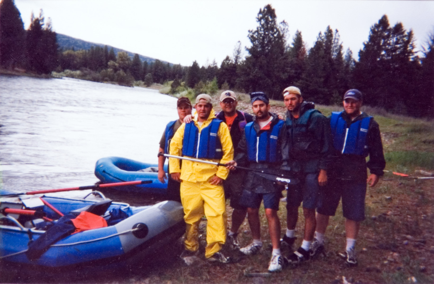 A group of six students in life jackets standing next to two rafts with rowing sticks.
