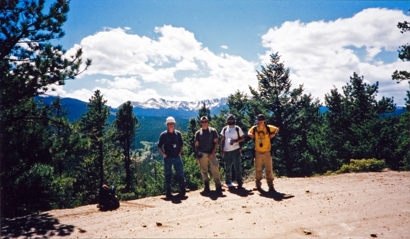 A group of four students that are standing in front of a mountain on a hiking trail.