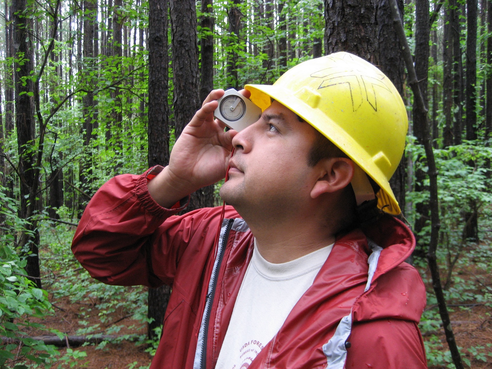 A student wearing a yellow hardhat looking into the sky through a tool.