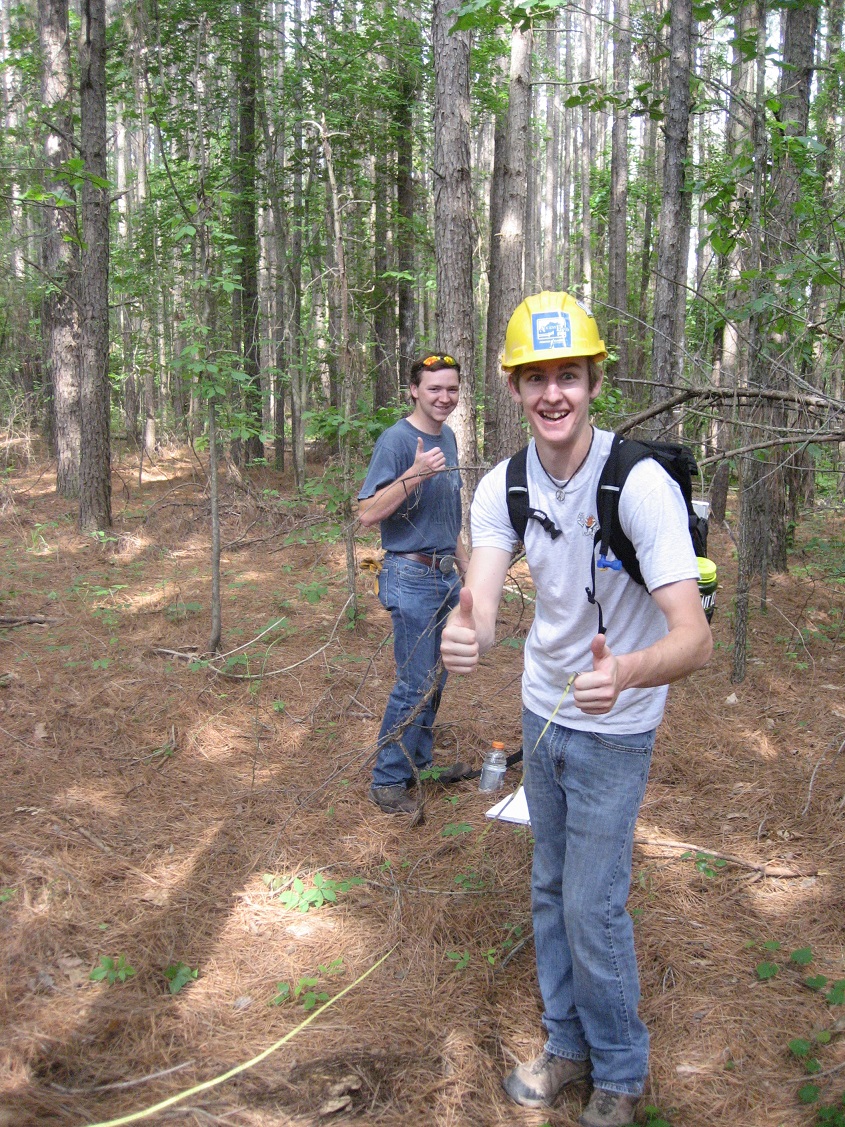 Two students standing in a wooded area giving a 