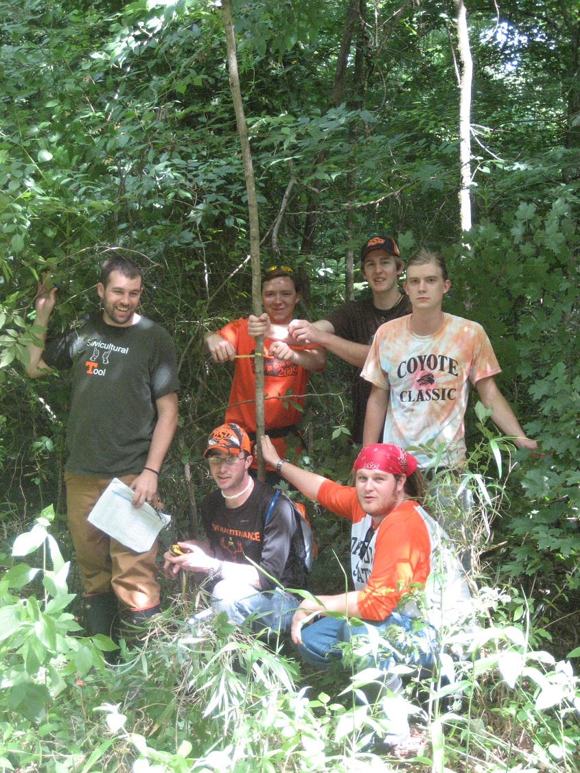 A group of students standing and kneeling in the forest. 