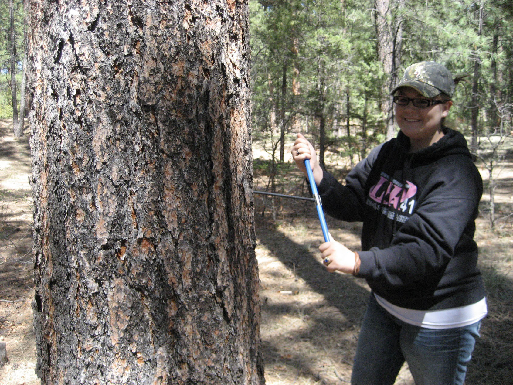 A student posing by a tree in the woods. A student posing by a tree in the woods.