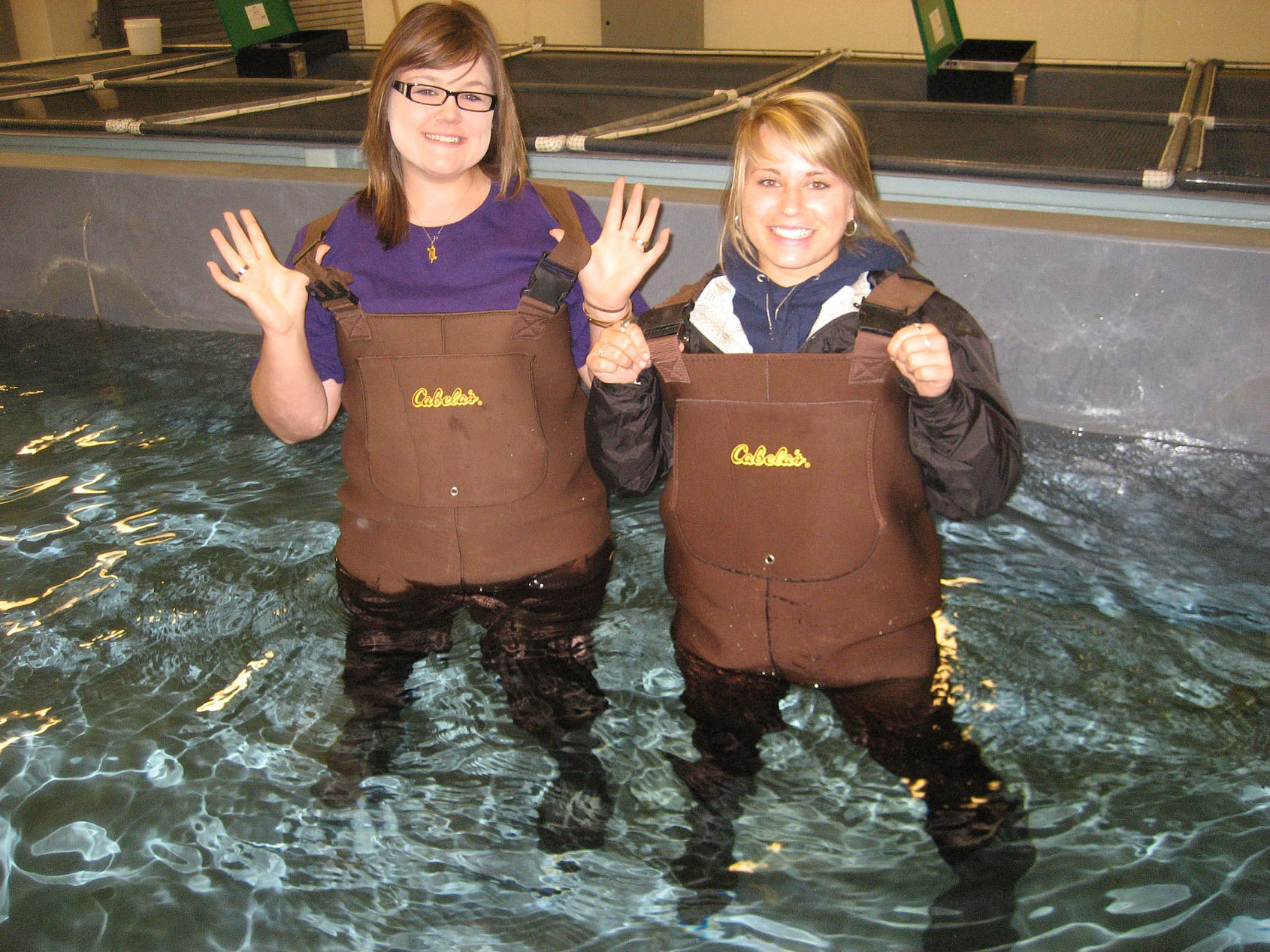 Two students posing in a tank of water with waders on. Two students posing in a tank of water with waders on.