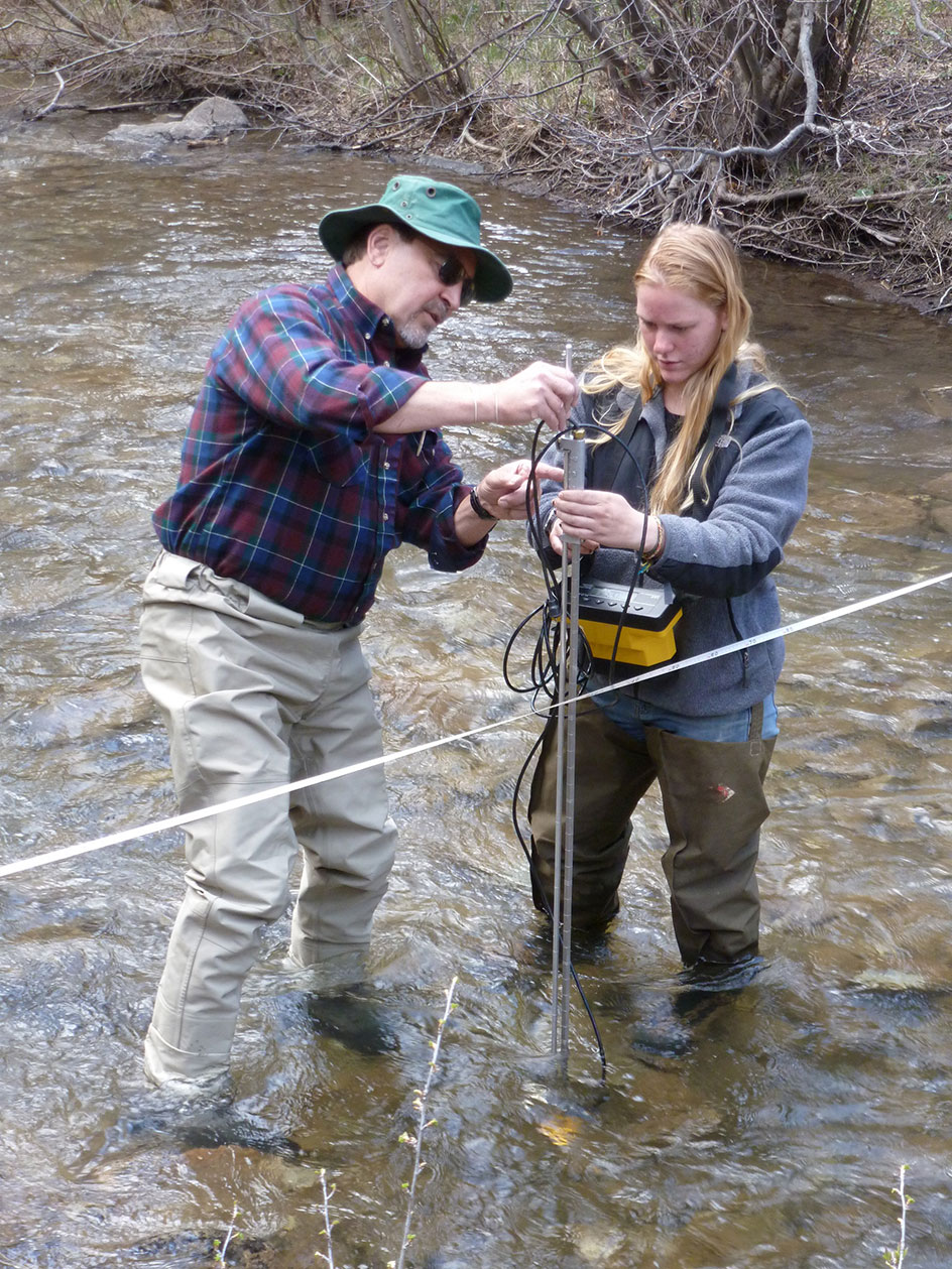 Two participants standing in a stream setting a post and string across the stream. 