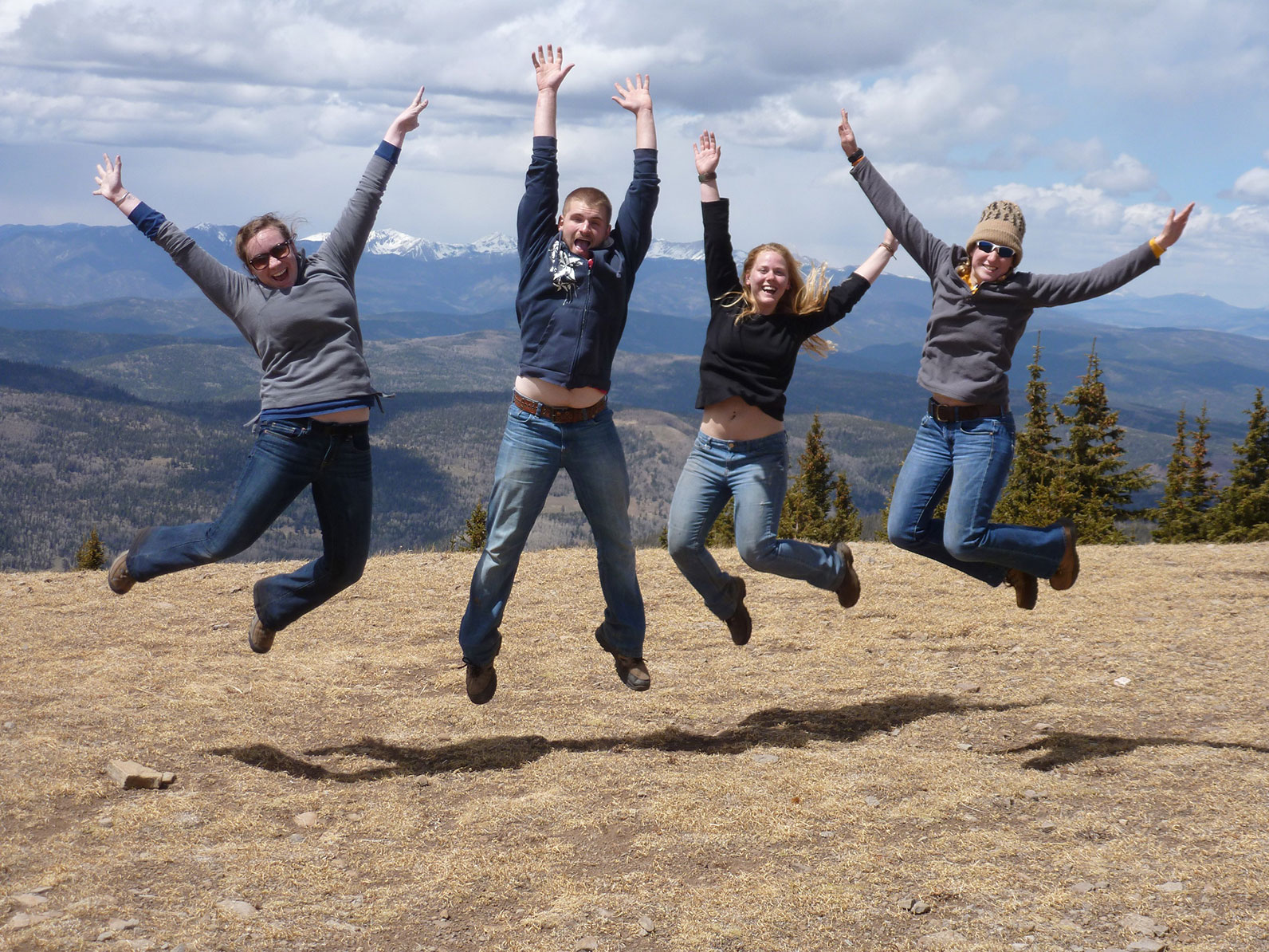 A group photo of four participants jumping for a photo overlooking a mountain range. 