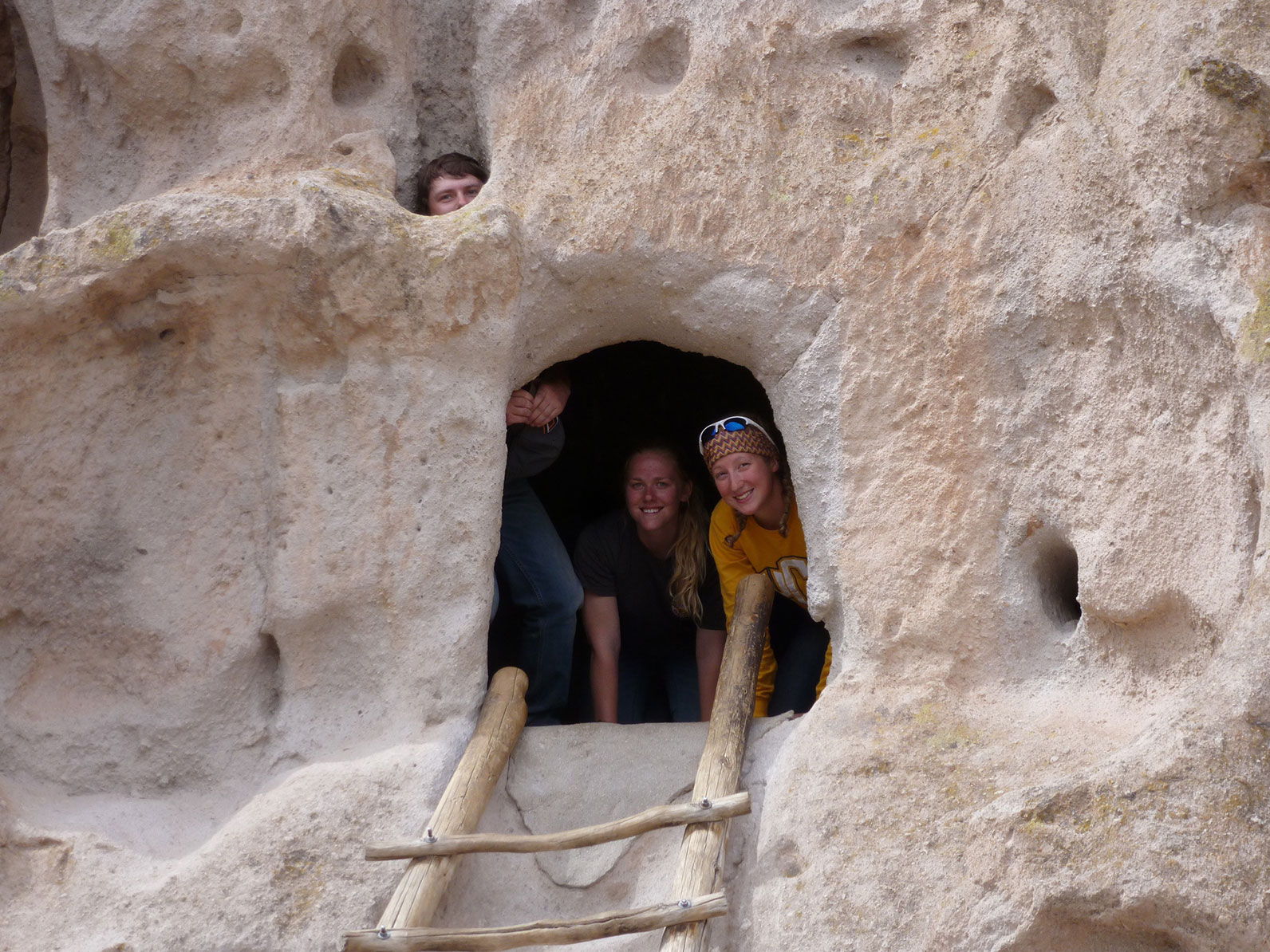 A group of three participants posing around a rock wall with an opening as a door. 