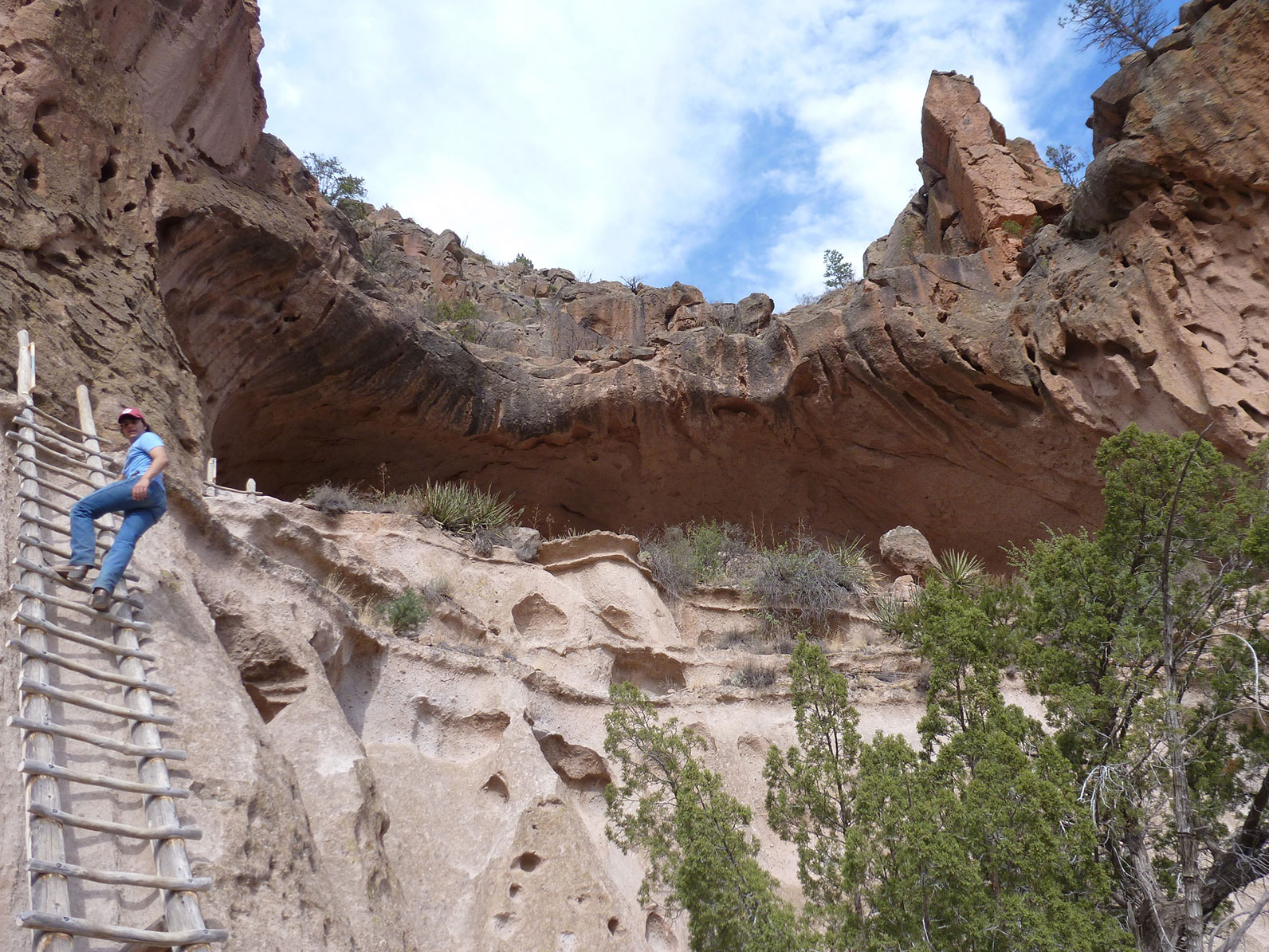 A student climbing a tall ladder up to caves in the side of a mountain. 