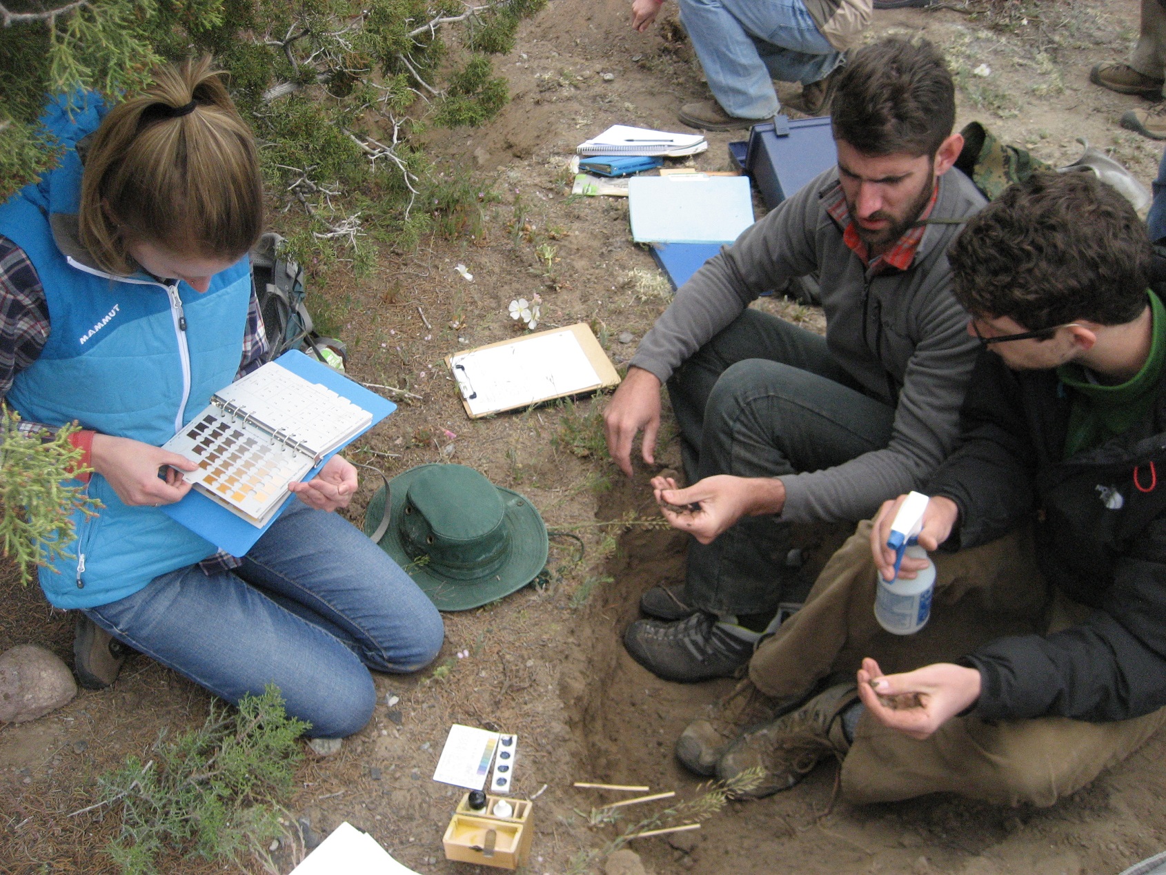 Three people sitting on the ground with papers and clipboards collecting information. 