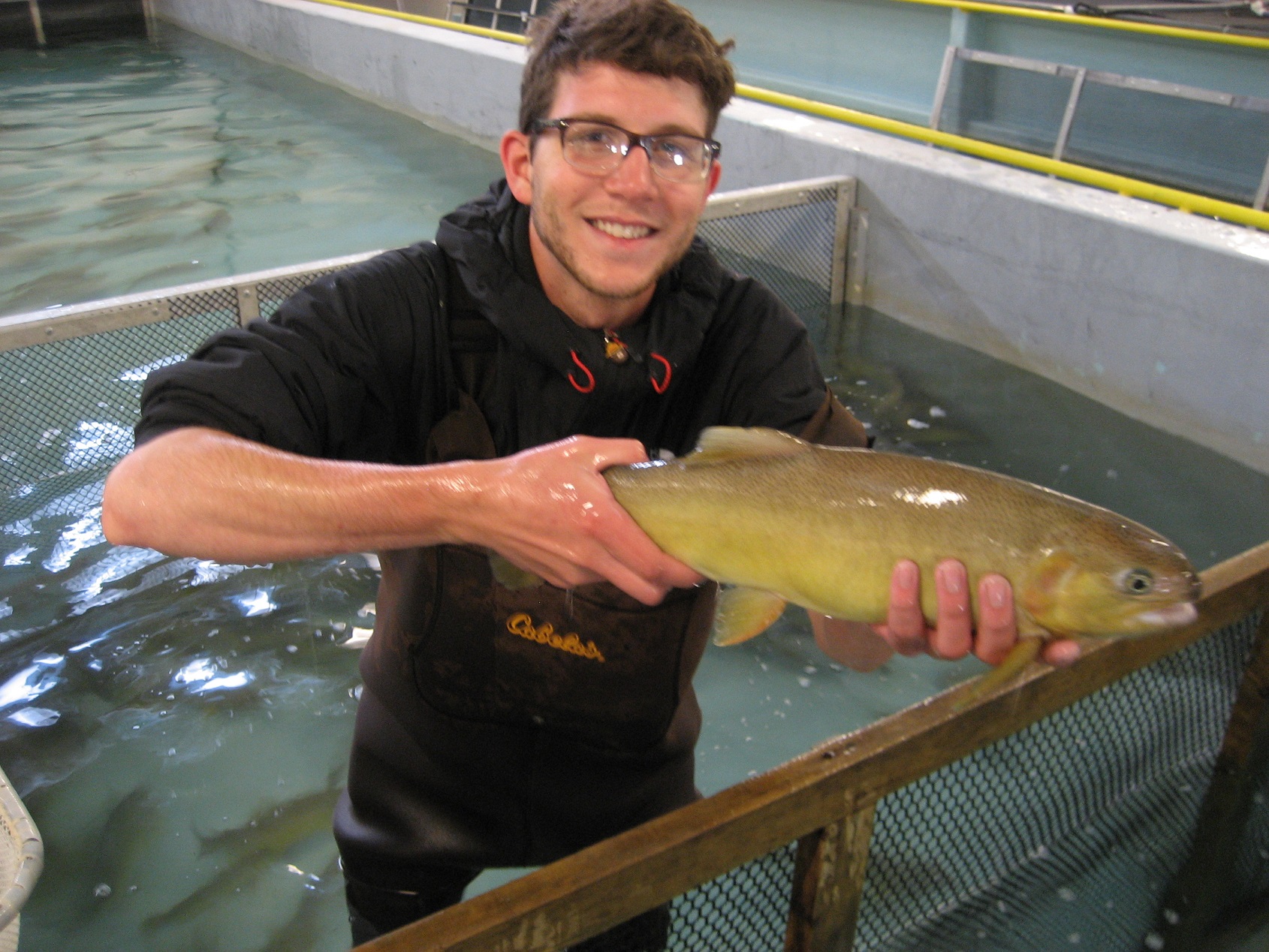 A participant standing in an indoor tank, with waders on, holding a fish up for the camera.
