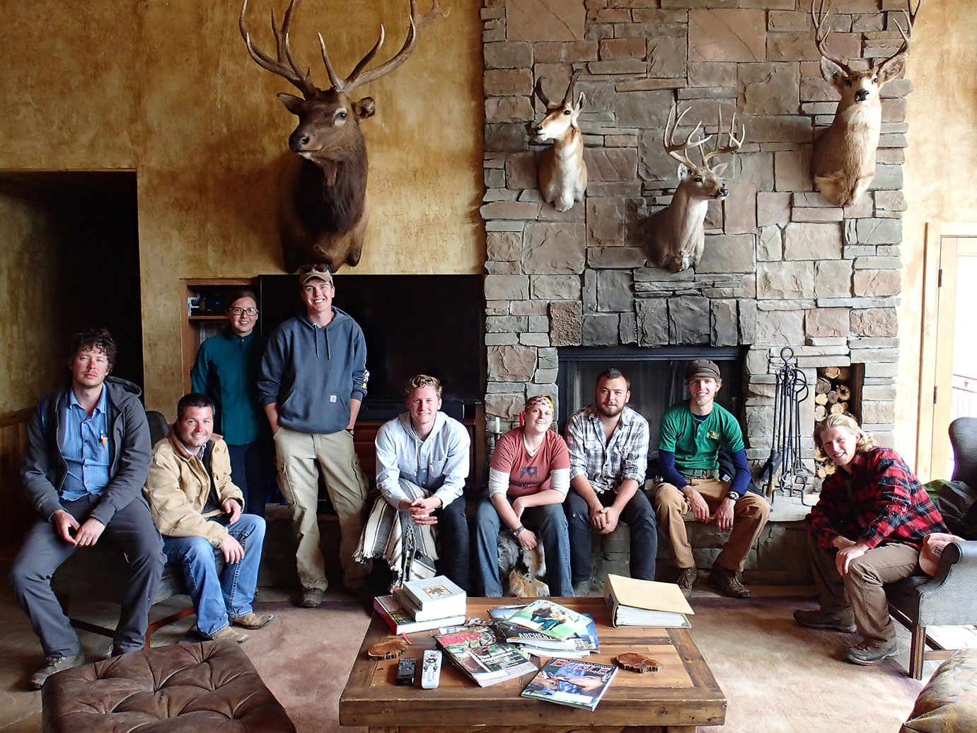 A group photo of nine people hanging out inside a lodge by a fireplace. 