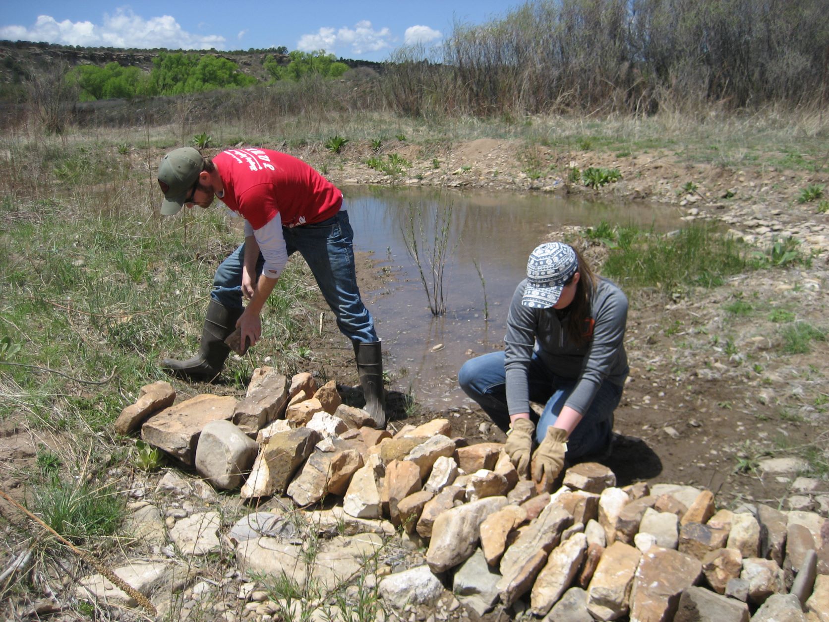 Two individuals arranging rocks beside a small pond in a valley. Two individuals arranging rocks beside a small pond in a valley.