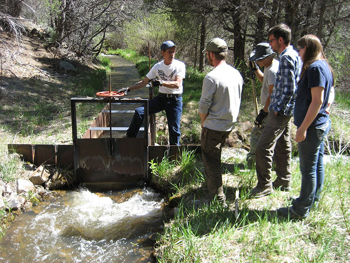 Four students receiving information from an instructor over a stream with a manual dam device. Four students receiving information from an instructor over a stream with a manual dam device.