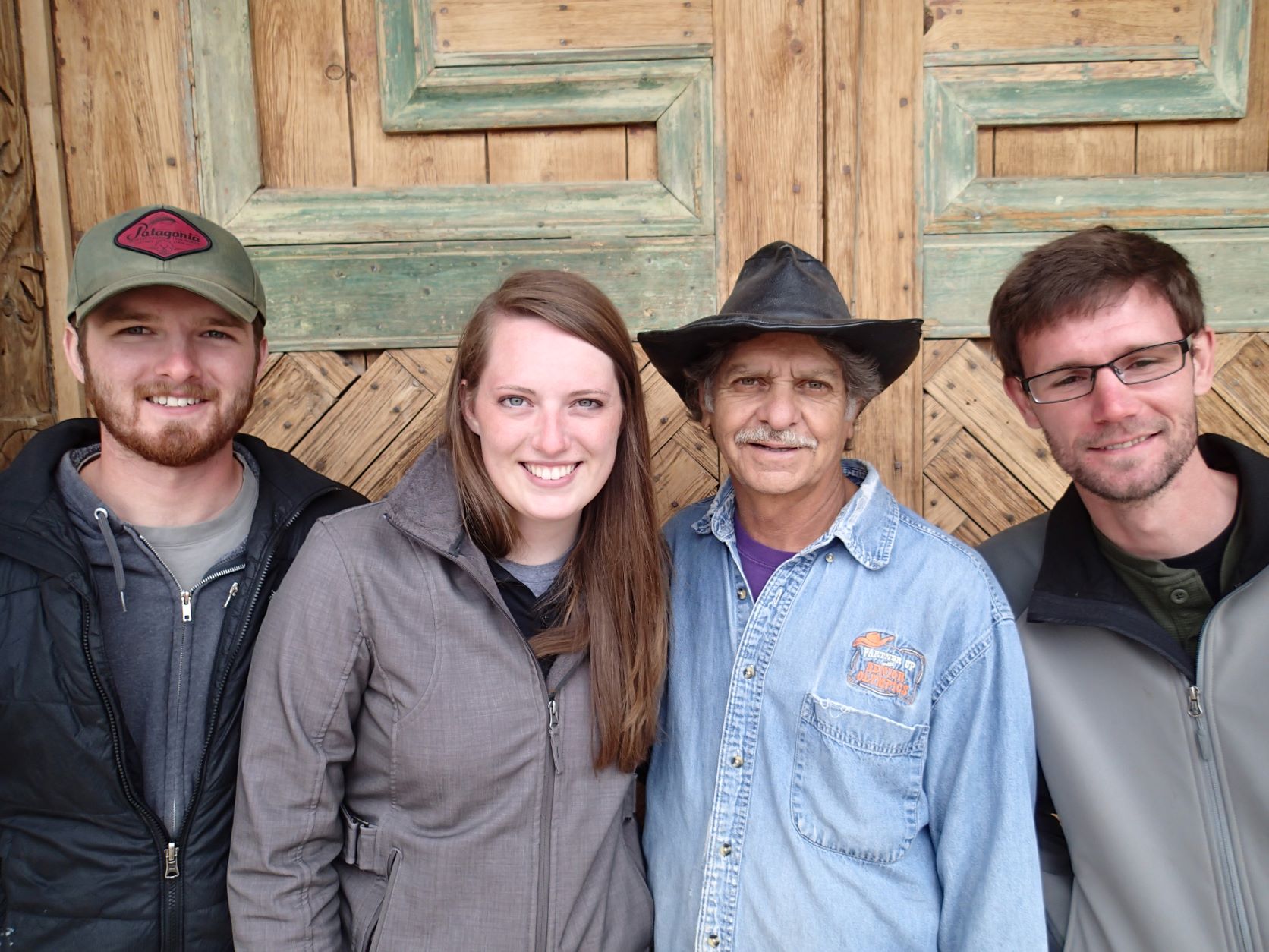 Four people standing, smiling at the camera, in front of the door. Four people standing, smiling at the camera, in front of the door.