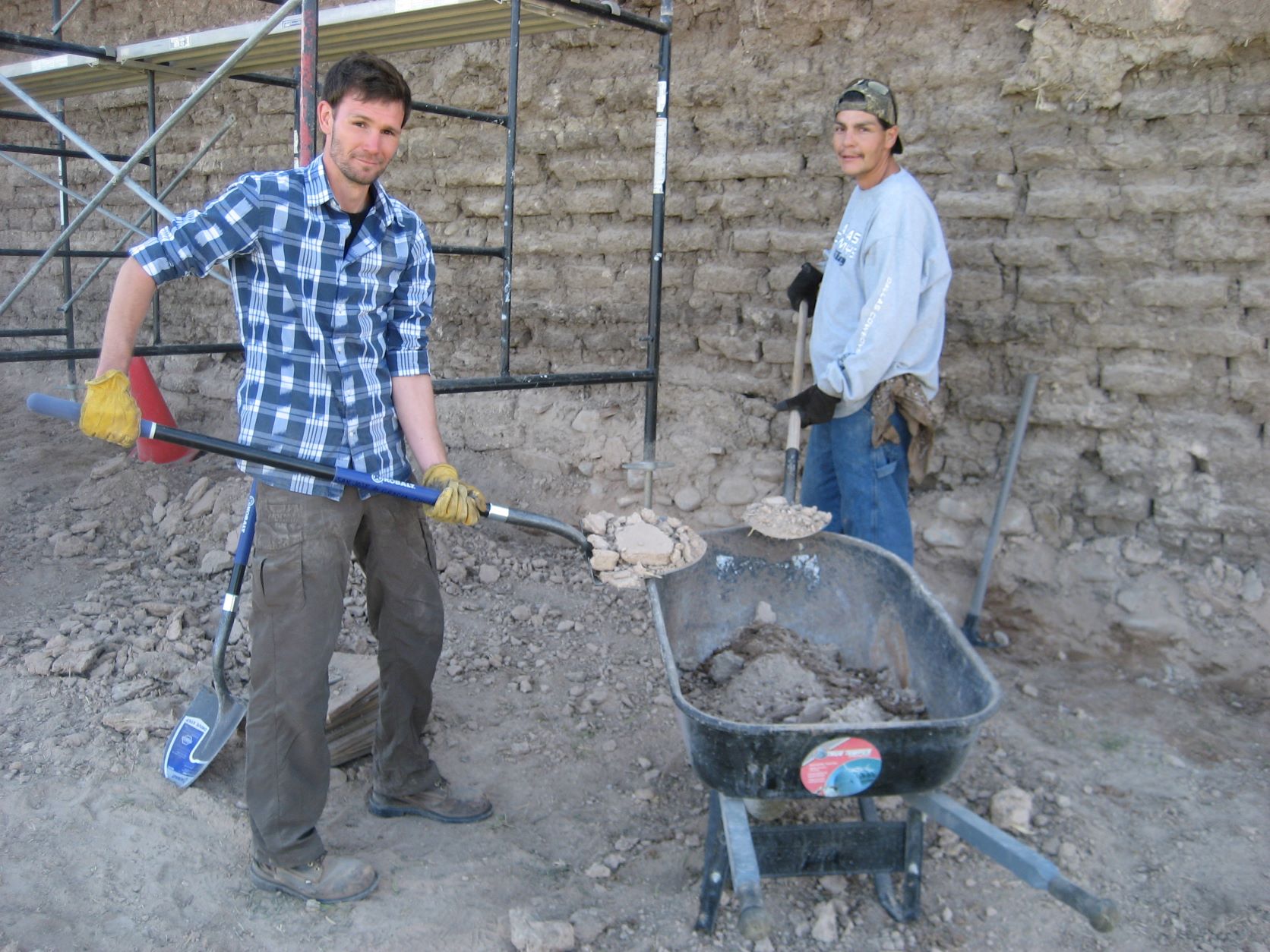 Two guys shoveling dirt and rocks into a wheelbarrow. Two guys shoveling dirt and rocks into a wheelbarrow.