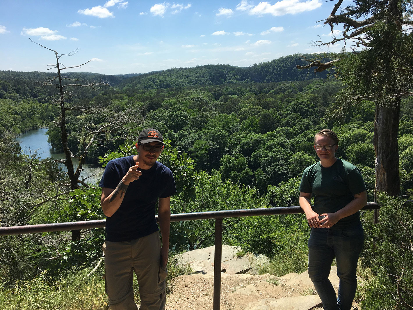 Two individuals standing in a forest, over looking a stream, posing for the camera. 