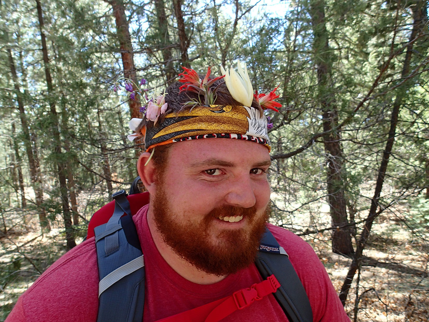 Participant posing in a forest with a bandana on with several flowers stick into it. 