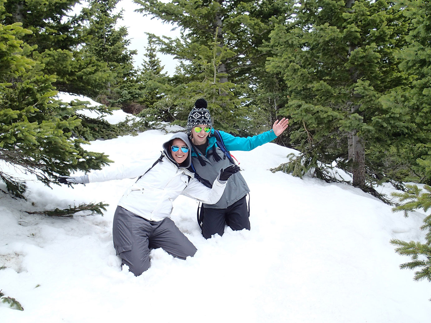 Two people smiling and posing in the snow in a forest. 