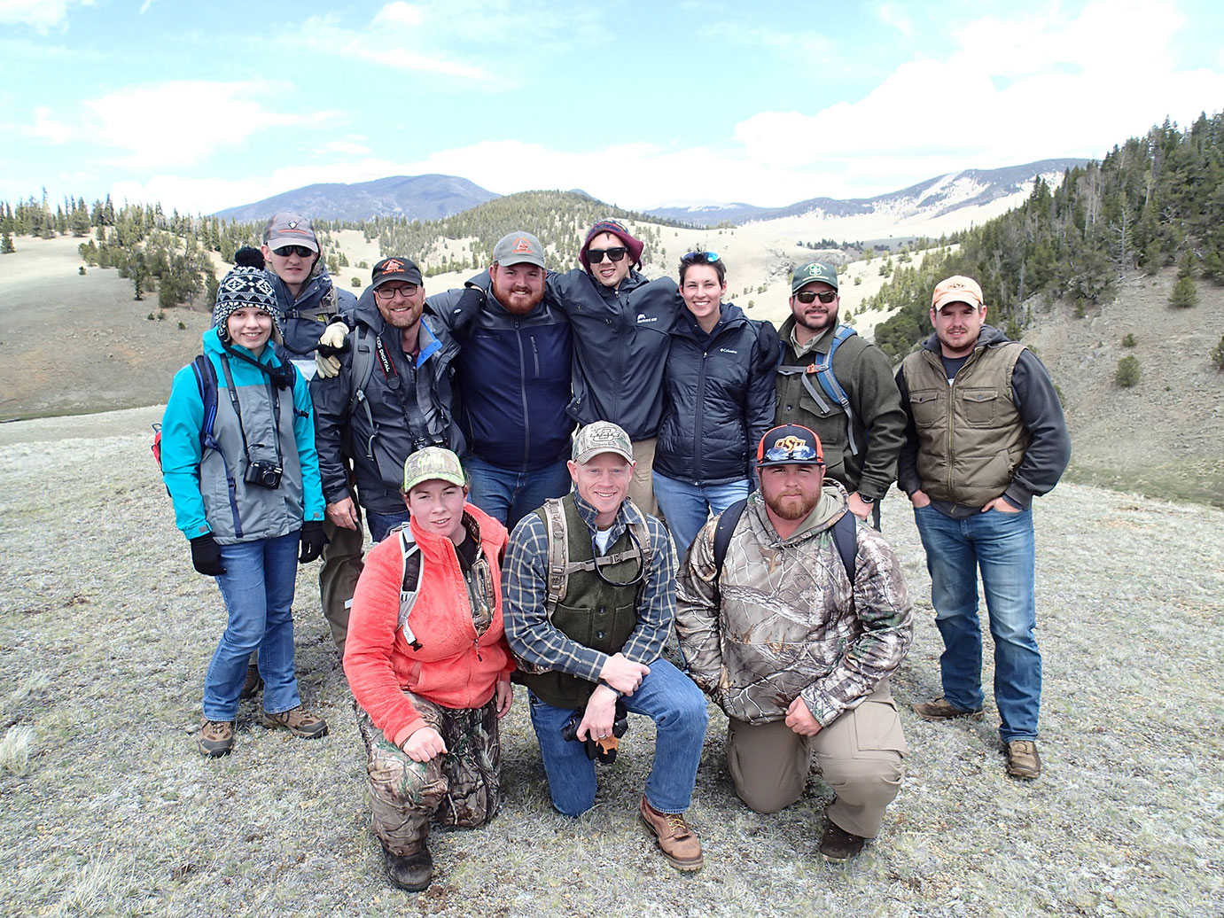 A group photo of eleven people standing in a valley of a mountain range. 