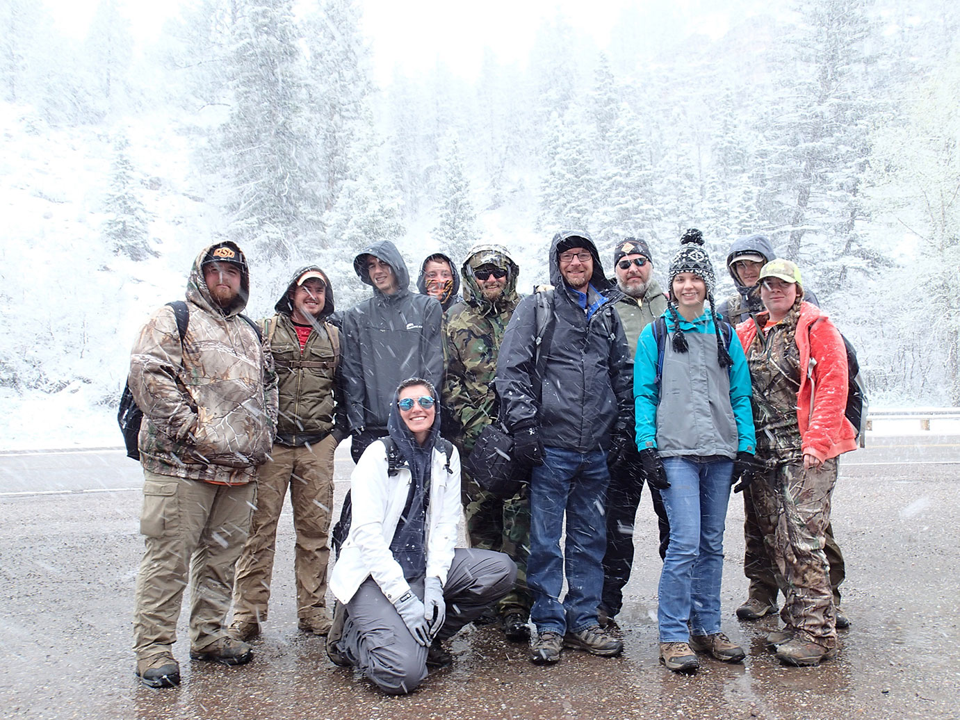 A group photo of eleven people standing in the snow in a forest. 