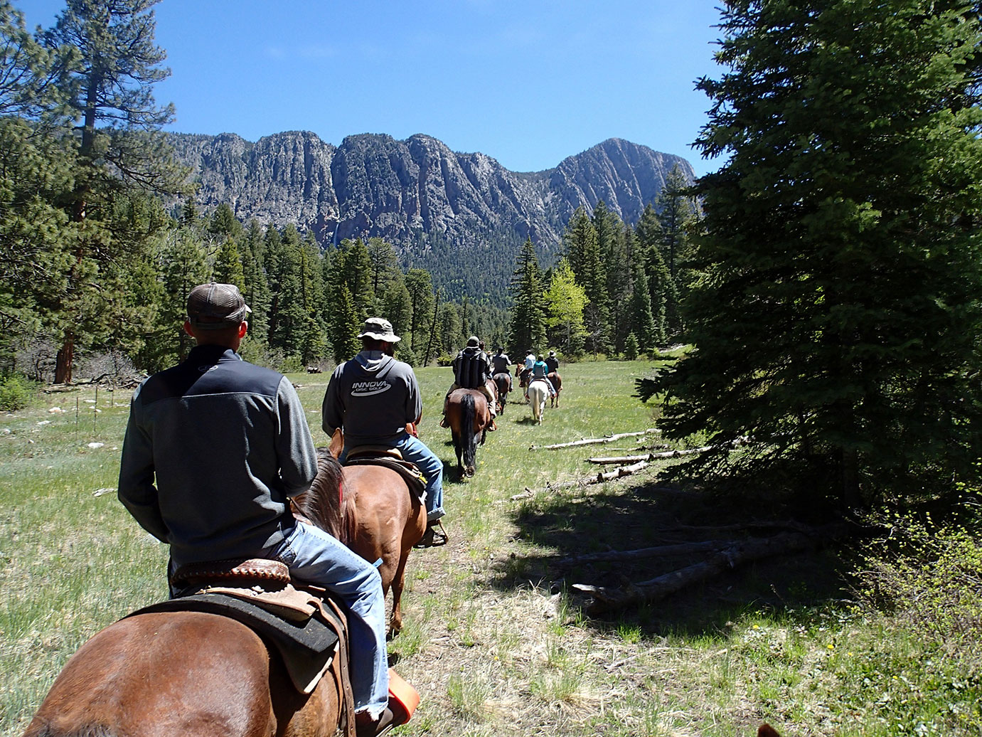 A group photo of people riding horses in a valley towards a mountain.