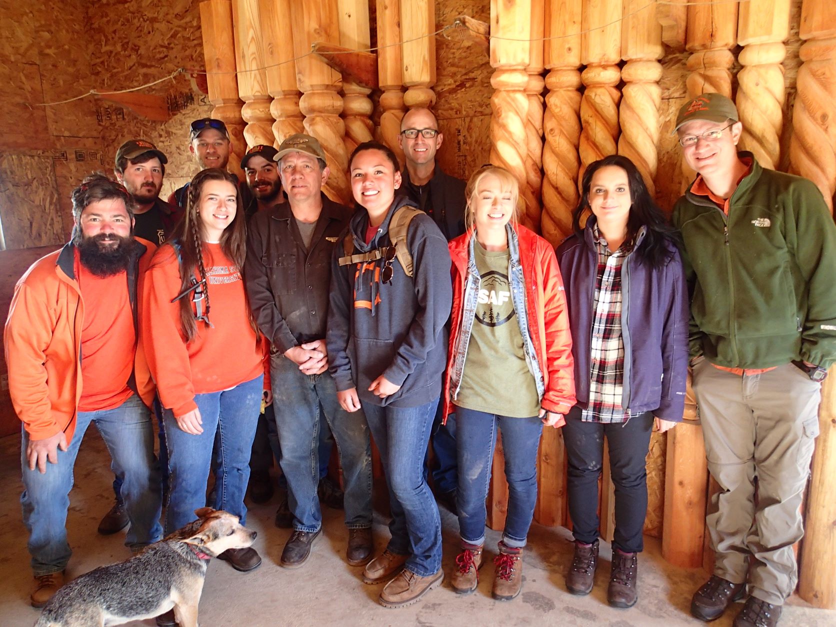 A group of 11 people standing in a room with carved wooden posts behind them. 