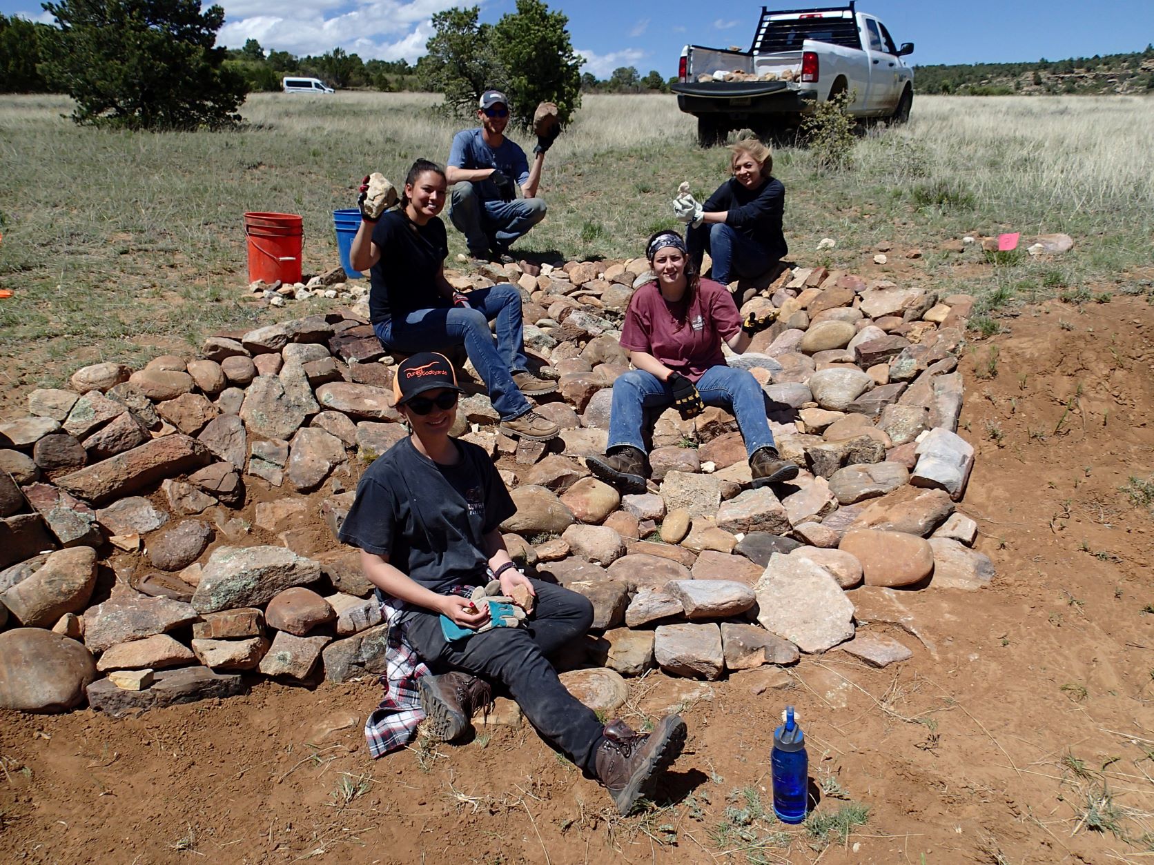 A group of five students sitting on a pile of medium sized rocks in a valley. 