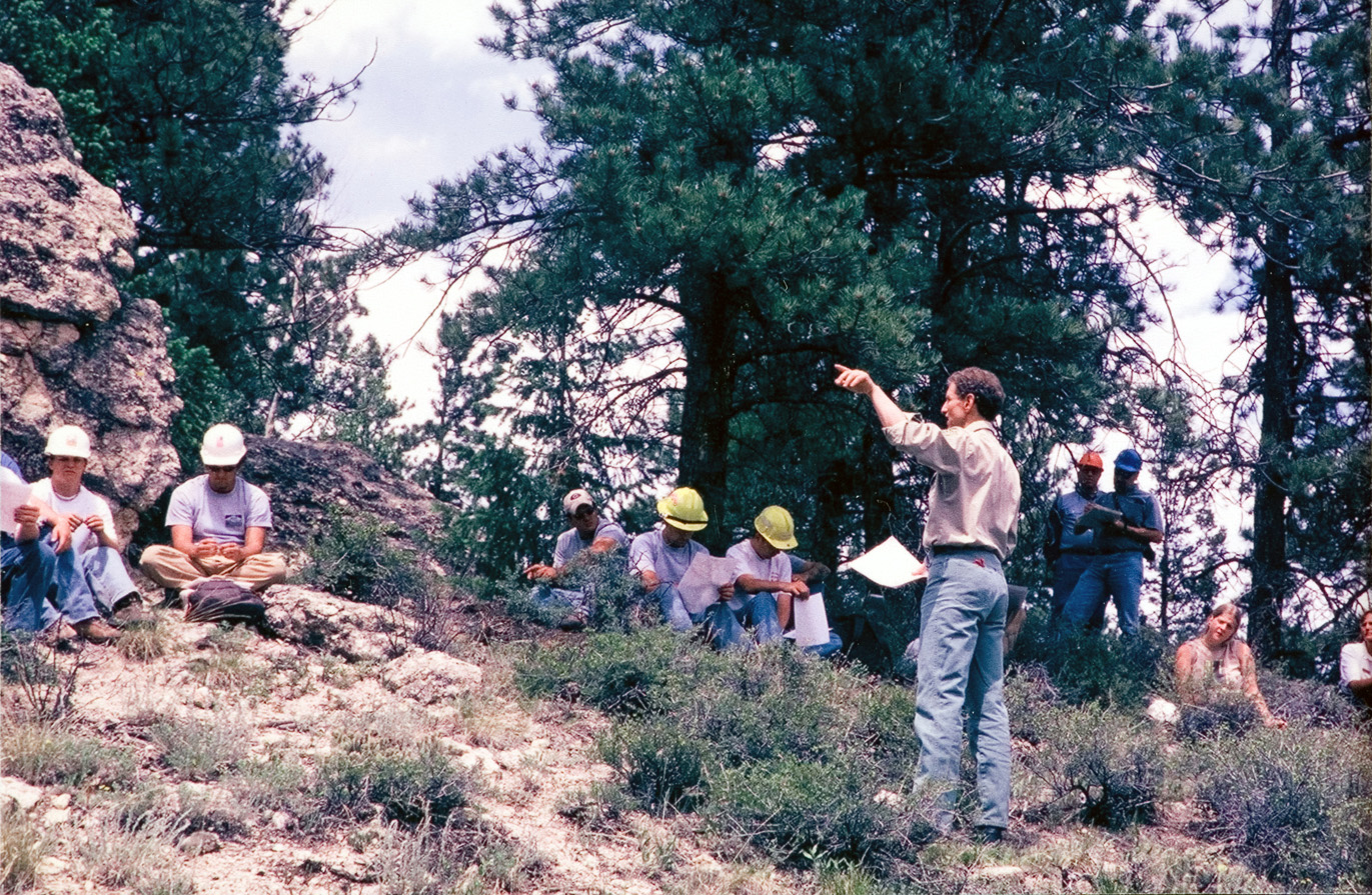Students rest on a rocky hill while listening to the instructor.